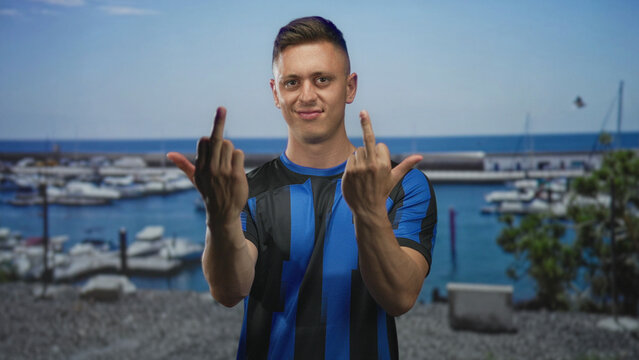 Man shows middle finger with bare hands on street near marina boats and pier; defiance rivalry fan team.