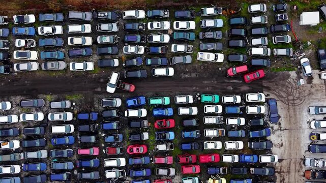Drone perspective of dismantled cars. Wide aerial frame of rows of stripped vehicles with scattered wheels beside a paved access road.