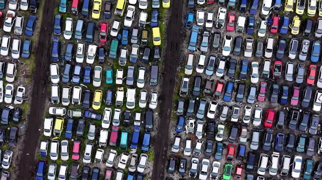 Vehicle graveyard. Dense grid of crushed and dismantled cars separated by narrow dirt paths and scattered debris.