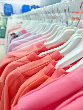 Colorful baby clothes on hangers in a store, neatly arranged in shades of pink, coral, and lavender.
