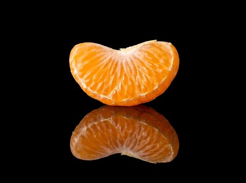 Single segment of a peeled mandarin orange fruit isolated on a black background with reflection