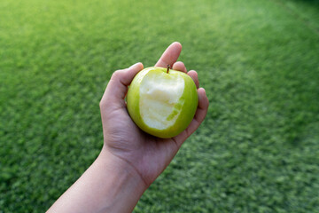 Hand Holding a Fresh Green Apple with Bite Mark on Natural Green Background. © JORGE DE LEÓN