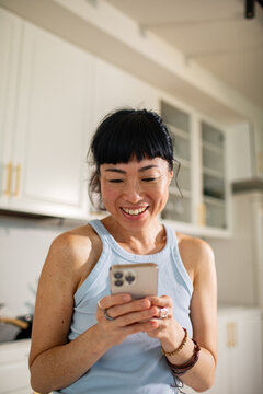 Smiling woman texting on smartphone in bright home kitchen