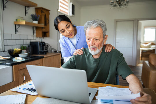 Caregiver assisting senior man with online bills at home