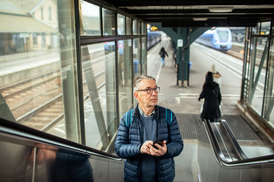 Senior man using smartphone on escalator at train station