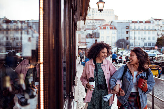 Two friends laughing with coffee on european city street