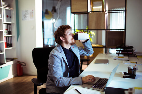 Young businessman drinking coffee at laptop in modern office