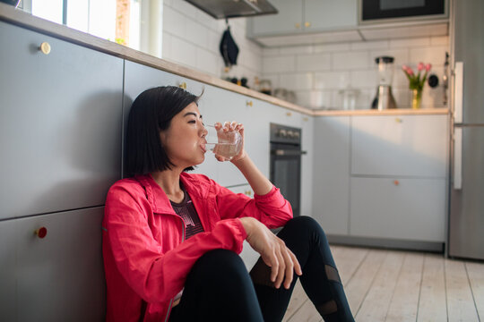 Young woman drinking water after workout in home kitchen