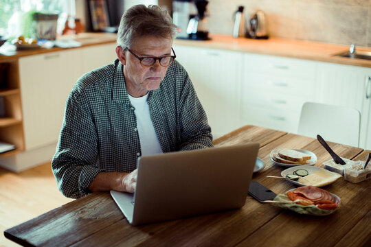 Senior man using laptop at kitchen table