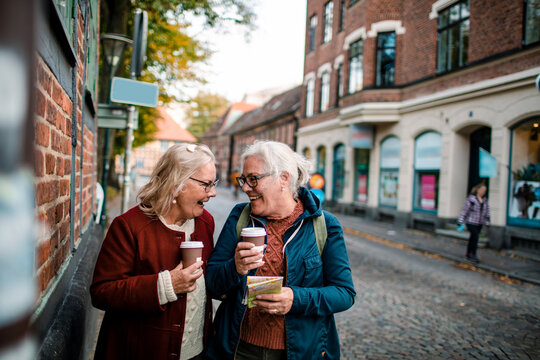 Senior women friends drinking coffee and reading map on old town street