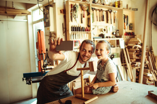 Father and daughter taking selfie in woodworking workshop