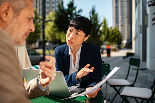 Two business professionals discussing paperwork at an outdoor city cafe