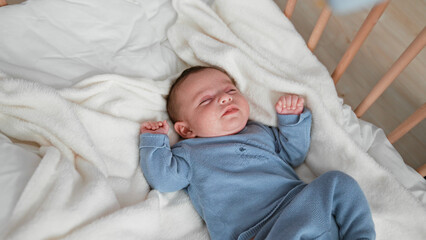 Baby boy sleeping with clenched fists and curled legs in a blue knit outfit on a white fleece blanket inside a wooden crib  gentle serenity. © Krakenimages.com
