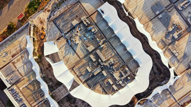 Aerial view showcases a modern building with unique shapes and structures. The scene is set during daylight in an urban environment with surrounding streets.