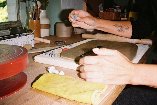 Tattooed hands working clay at a ceramics studio worktable