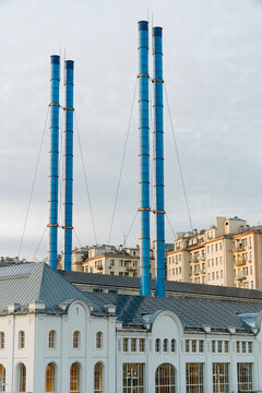 The front of a classical white factory with blue pipes in sunset.
