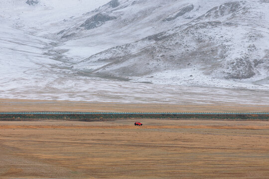A Red SUV, Highway, Snow Mountains, and Wilderness.