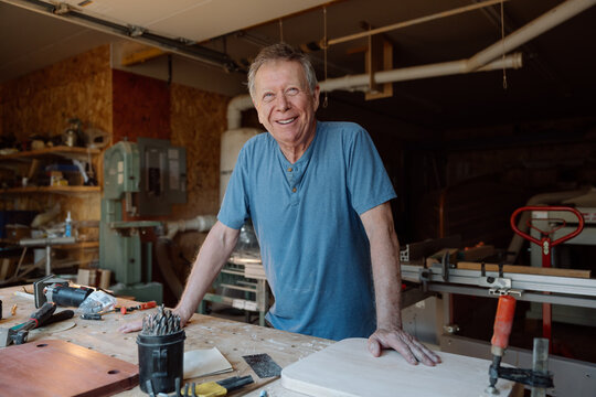 Smiling senior woodworker in workshop leaning on workbench