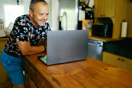 smiling retired man in his home with laptop in kitchen