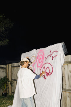 Man painting pink graffiti on sheet at garden night party