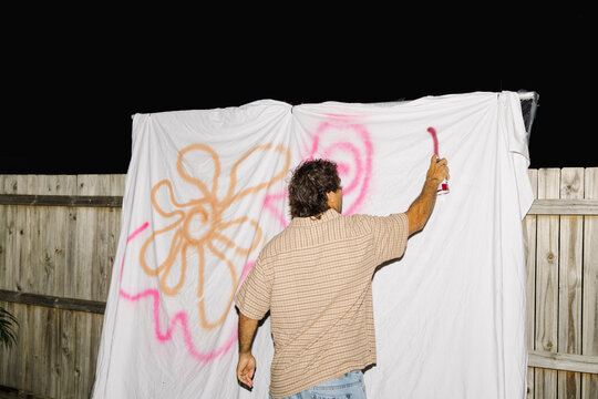 Man spray painting graffiti on sheet at backyard night party
