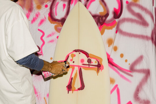 Man spray painting mushroom design on surfboard at night