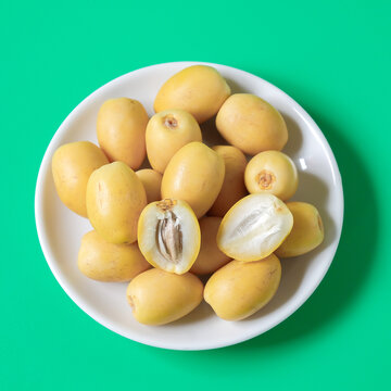 Fresh yellow dates palm fruit on white dishwasher.