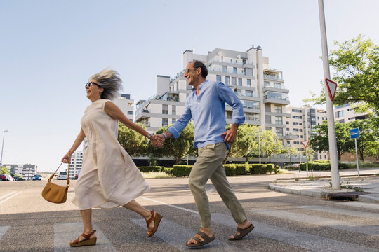 Senior couple running hand in hand across street in summer