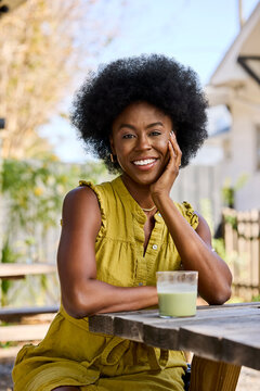 Afro Woman Sits at a Table With a Green Drink