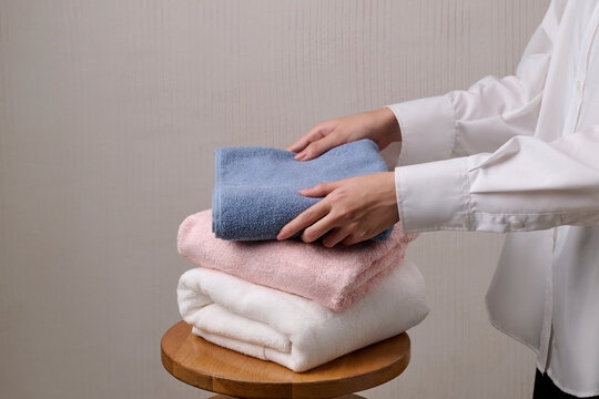Hands folding neatly stacked soft fluffy towels in pastel colors
