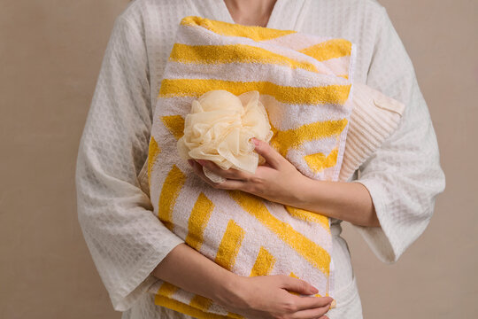 Woman in bathrobe holding fluffy bath sponge and striped towel