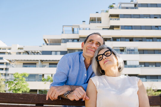 Senior couple leaning together on bench outside luxury apartments