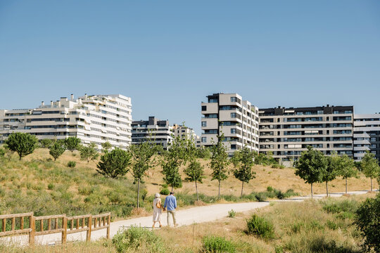 Anonymous senior couple walking through park near luxury apartments