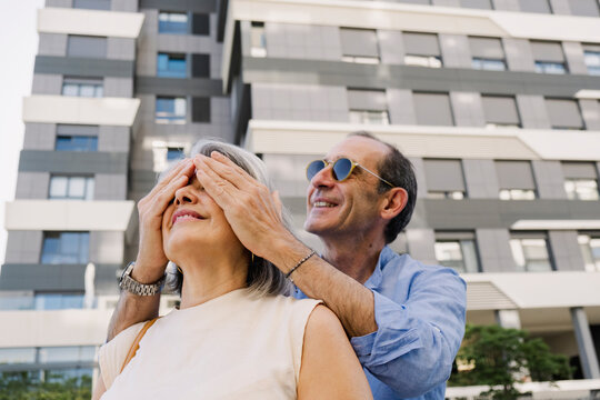 Senior man covering woman&acirc;s eyes outside luxury apartments