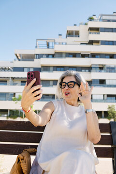 Senior woman waving on video call outside luxury apartments