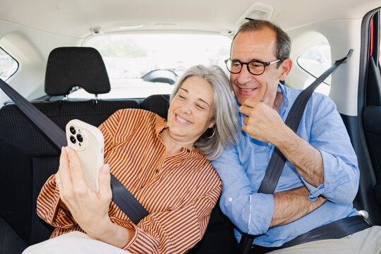 Mature senior couple smiling at smartphone in back seat of car