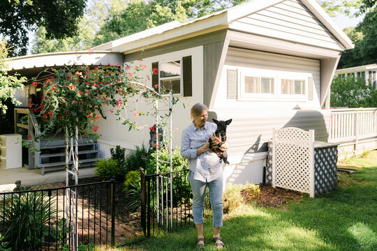 portrait woman holding her dog in front of her home