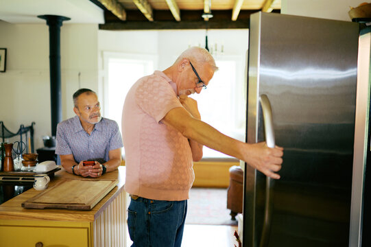 couple at home in their kitchen, talking while looking in fridge 