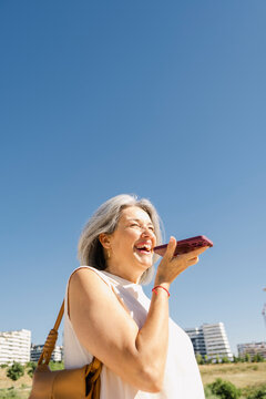 Mature senior woman laughing while using voice message app blue sky