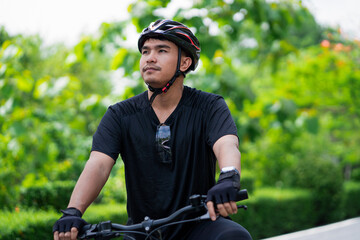 Fototapeta premium Young Asian Male Cyclist Looking Ahead While Riding Bicycle in Green Park Promoting Focus, Outdoor Exercise, Healthy Lifestyle, Endurance, Cycling, and Active Recreation
