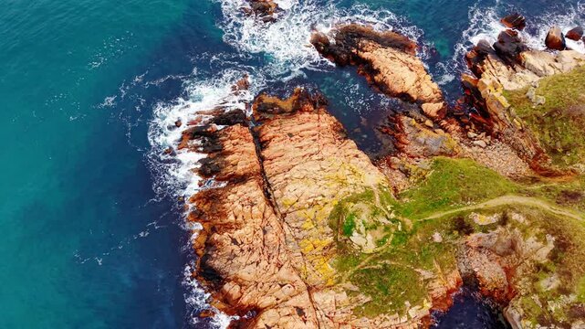Aerial view of red rock cliff along Black Sea coast, Bulgaria. Overhead drone shot of textured stone ledge, green meadow and breaking wave below.