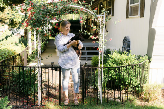 portrait of woman holding her dog in front of her home