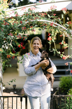 portrait of woman holding her dog in front of her home