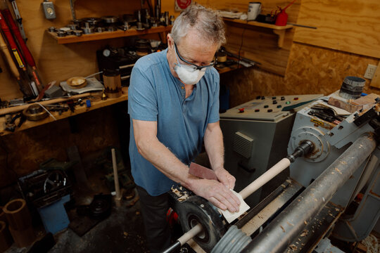Older woodworker sanding a lathe-turned spindle 