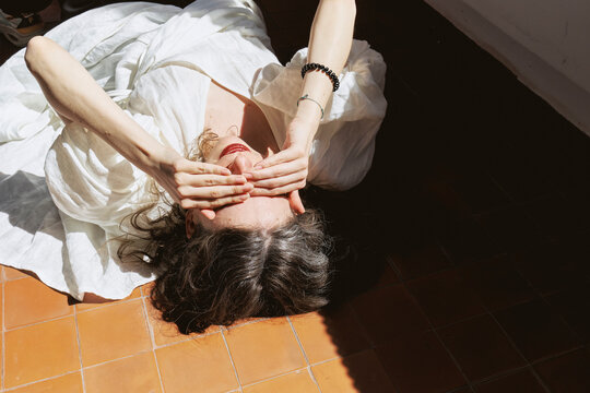 Young woman relaxes on studio floor with eyes covered by hands