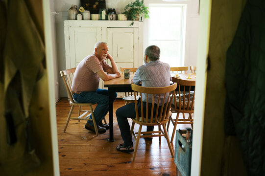 retired gay couple relaxing at home and sitting by dining table