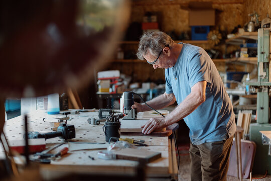 Senior woodworker focused on routing a wooden board in workshop