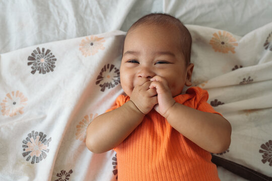 Happy smiling baby laughing on bed covering face