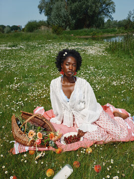Woman Sits on Picnic Blanket With Basket and Fruits in Green Field