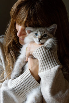 Woman cuddling blue-eyed kitten in cozy sweater, tender moment
